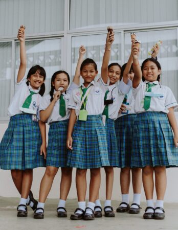 An image of six schoolgirls wearing teal plaid skirts and matching ties. They're all triumphantly holding up ice cream cones.